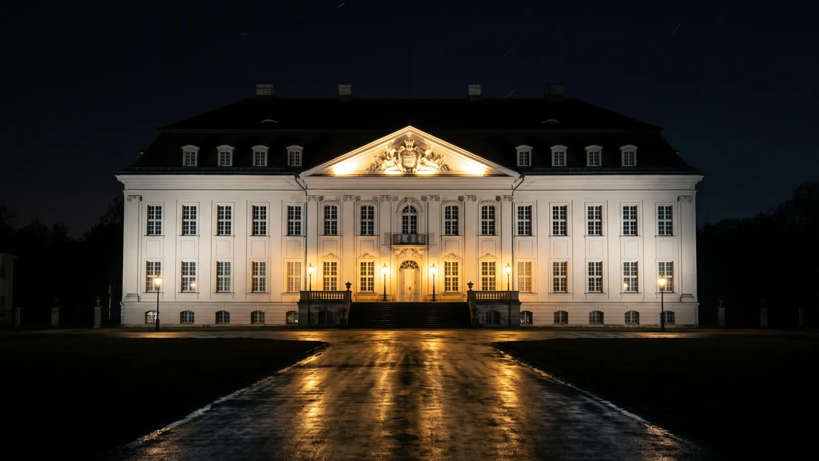 Schloss Friedrichsfelde bei Nacht, der weiße Barockbau hell angestrahlt vor schwarzem Himmel.